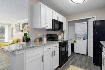 The galley kitchen with white cabinets and black appliances also has the laundry closet.